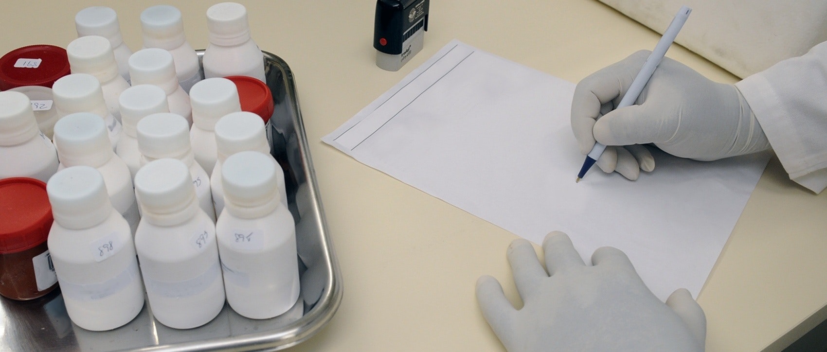 pair of hands writing near tray with medicines